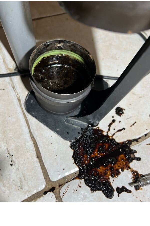 Dépôt de bistre liquide noir récupéré dans le té de purge d’un conduit de poêle à granulés, signe d’humidité et de mauvaise combustion.